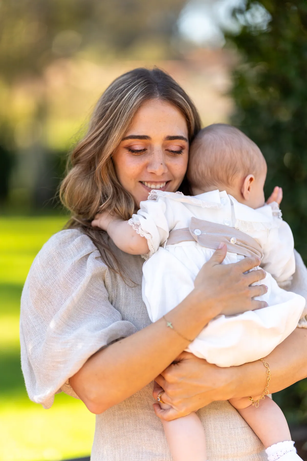 Mãe a sorrir com o bebé ao colo no dia do batizado