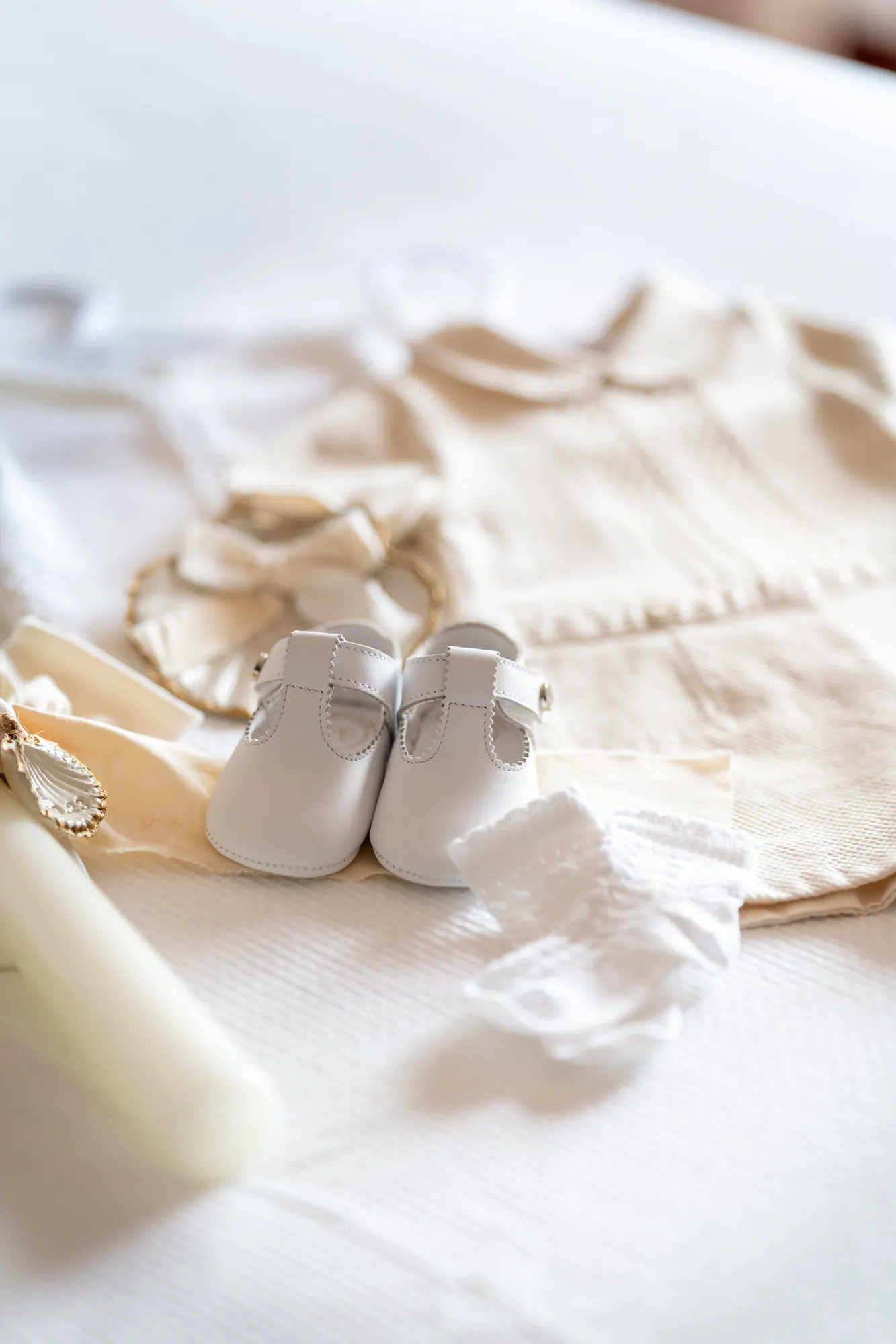 Sapatinhos de bebé brancos sobre a roupa de batizado e uma vela
