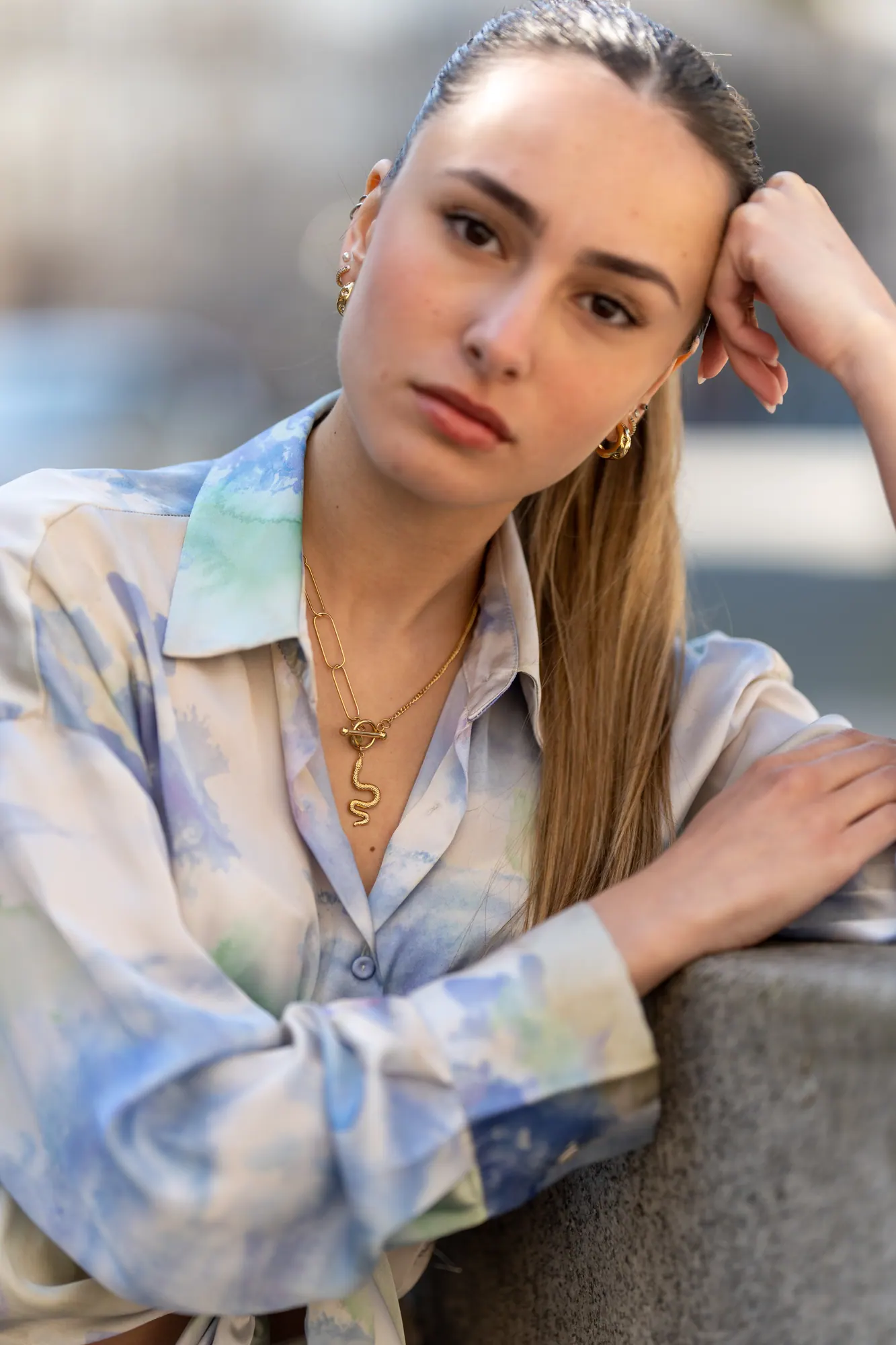 Modelo de camisa pastel e colar dourado, de cabeça apoiada na mão